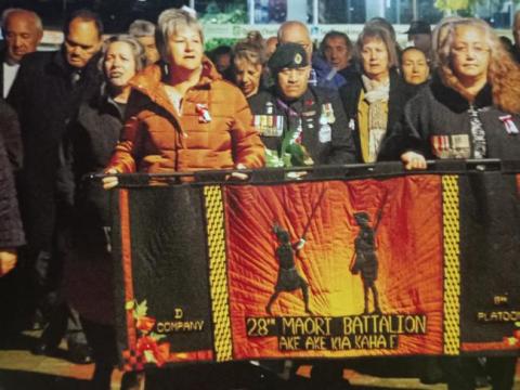 A crowd of people with a 28 Māori Battalion banner
