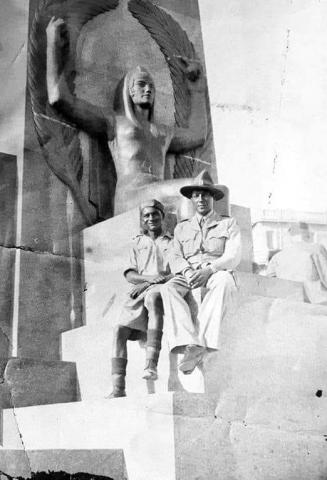 Two men seated in front of an Egyptian statue 
