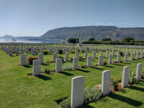 Rows of gravestones in green lawn with a bay in the background.